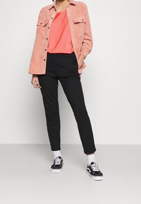 Korallfärgad kordjeansskjorta, svarta skräddarsydda byxor, svartvita sneakers, med vita strumpor. Enkla linjer, avslappnad passform och textilstruktur.