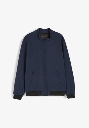 Granatowa kurtka bomberka z zapięciem na zamek, stójką, dwoma bocznymi kieszeniami oraz czarnymi ściągaczami na mankietach i u dołu. Gładka tekstura tkaniny.
