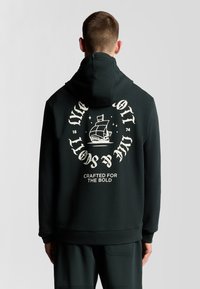 Felpa nera con cappuccio e cordino, caratterizzata da una grande grafica di una nave e testo sul retro. Realizzata in tessuto morbido con una vestibilità comoda.