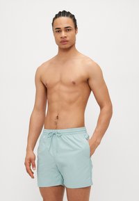 Shorts de bain bleu clair en tissu à séchage rapide. Comprend une taille élastique avec un cordon de serrage et des poches latérales. Design simple, sans motifs.