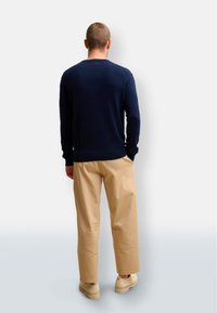 Mörkblå tröja med långa ärmar, ribbade muddar och nederkant, tillsammans med beige byxor och ljusa skor. Bakifrån visad.