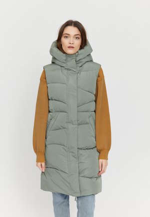 Grüne gepolsterte Weste mit hohem Kragen und übergroßer Kapuze, ausgestattet mit Seitentaschen und einem etwas längeren Schnitt, kombiniert mit einem braunen Pullover.