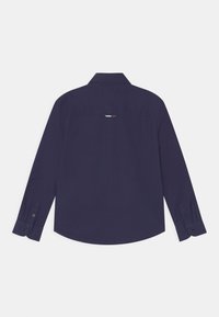 Granatowa koszula z długim rękawem, z wywijanym kołnierzykiem, z zapięciem na guziki przy mankietach oraz z przeszyciem na plecach. Materiał wydaje się gładki i trwały.