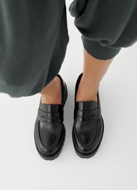 Svarte skinnloafers med glatt overflate, med en enkel rem som detalj og tykke, teksturerte gummisåler.