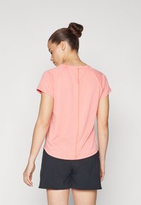 Rosa kortermet treningstopp med strukturert overflate, avrundet nederkant og kontrasterende sømmer, kombinert med mørke shorts.