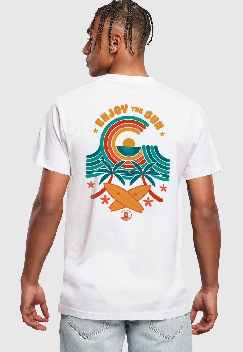 Hvit bomulls t-skjorte med en fargerik grafikk av bølger, sol, palmer og surfebrett. Tekst "NYT SOLEN" i fet oransje og teal.