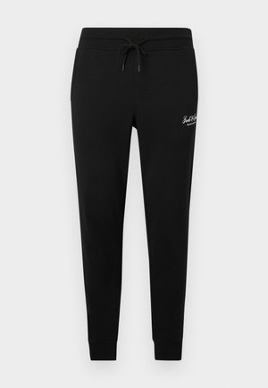 Schwarze Sweatpants mit schmal zulaufendem Bein, Kordelzug am Bund und kleinem weißem Logo am oberen linken Oberschenkel.