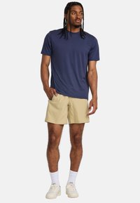 Camiseta de manga corta azul marino combinada con pantalones cortos beiges. Tejido texturizado y corte relajado. Llevada con calcetines blancos y zapatillas ligeras.