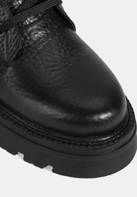 Botte en cuir noir avec une finition texturée, bout rond, semelle en caoutchouc noir solide et lacets noirs. Couture visible le long du bord de la semelle.