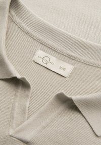 Polo shirt de un beige claro confeccionado en tejido texturizado. Presenta un cuello clásico y una etiqueta de marca con el texto "quintessence" y la talla "M."