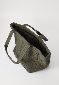 Oliven grønn quiltet totebag med et geometrisk mønster, med korte håndtak og en glidelåslomme innvendig. Teksturert stofffinish.