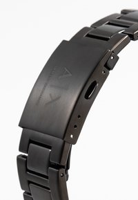 Svart armbandsur i rostfritt stål med matt yta, rektangulär urtavla, länkarmband och ingraverad logotyp. Utrustad med ett viklås och justeringshål.