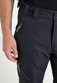 Pantalons techniques noirs en tissu durable avec des poches zippées dotées de poignées en cuir et d'une finition texturée pour une meilleure adhérence.