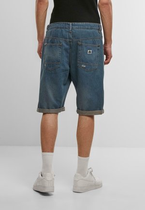 Lysblå denimshorts med opkridt kant, der har to baglommer og et logo patch. Parret med hvide sneakers og ankelstrømper.