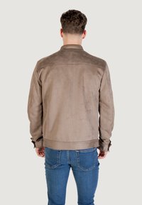 Giacca in suede marrone con colletto semplice, polsini con bottoni e una texture liscia, indossata con jeans blu, vista da dietro.