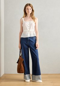White lace tank top with button detail and tie waist, paired with wide-leg blue denim jeans featuring frayed cuffs and white sneakers. Brown bag included.