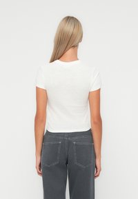White cotton t-shirt with short sleeves, round neckline, and a cropped fit, paired with high-waisted dark gray jeans featuring visible pocket seams.