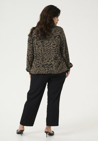 Leopardenmuster-Bluse in erdigen Tönen, mit langen Ärmeln und lockerer Passform. Kombiniert mit schwarzen, maßgeschneiderten Hosen und High Heels.