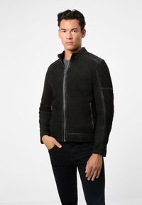 Schwarze Wildlederjacke mit Stehkragen, Reißverschluss, zwei seitlichen Taschen und kontrastierenden Nähten an den Schultern. Glatte Textur.