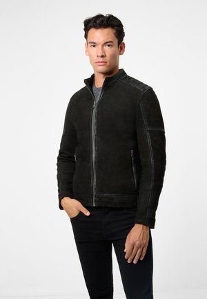 Veste en daim noir avec un col montant, fermeture éclair, deux poches latérales et des coutures contrastées le long des épaules. Texture lisse.