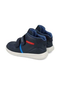 Zapatillas altas de color azul marino con suelas blancas, detalles en rojo y azul, y correas ajustables de Velcro sobre un fondo blanco.