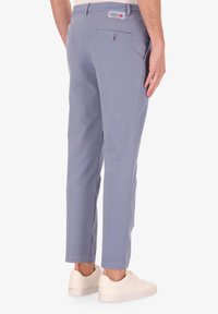 Pantaloni azzurri chiari realizzati in un tessuto morbido, con una tasca posteriore con bottone e un'etichetta di marca sulla vita. Abbinati a sneakers bianche.