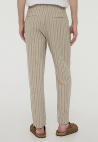 Pantaloni a righe beige con vestibilità slim, dotati di tasche posteriori e una trama sottile; abbinati a scarpe marroni senza lacci.