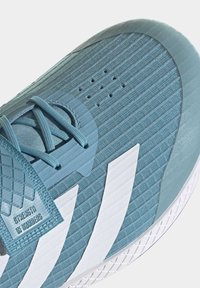 Botte de sport bleue avec un tissu texturé, un motif rayé, un logo à trois bandes blanches et une zone de orteil renforcée. Comprend des lacets et des trous d'aération.