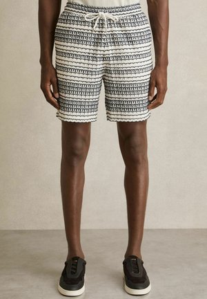 Strickshorts mit schwarz-weißen horizontalen Streifen, ausgestattet mit einem Kordelzugbund und strukturiertem Saum. Kombiniert mit schwarzen Sneakers.