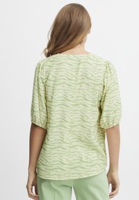 Blusa a maniche corte di colore verde chiaro con un motivo ondulato. Presenta un tessuto morbido e texturizzato e maniche a sbuffo elasticizzate, orlo arrotondato.