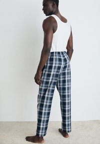Pantalons de pyjama en coton à carreaux bleu marine et blanc, avec une taille élastique et une coupe décontractée. Portés avec un débardeur blanc, pieds nus.