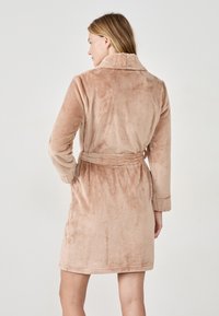 Accappatoio plush marrone chiaro con colletto a scialle, vita con cintura e maniche lunghe. Il tessuto ha una finitura morbida e testurizzata.