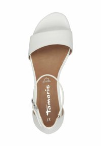 Vit sandal med ett brett band över framsidan, ett tunt ankelband och en klossklack. Slät textur med en vadderad sula.