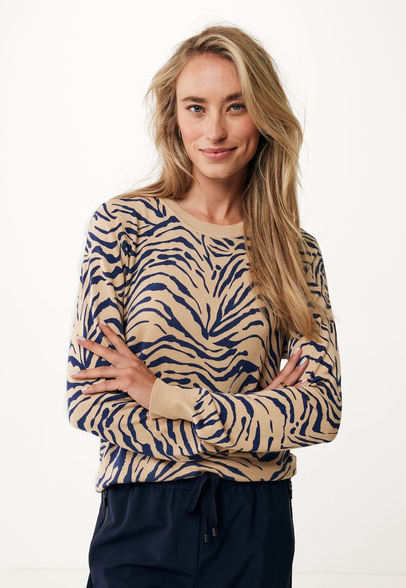 Beige tröja med marinblå tigerstrimmönster, rund hals och långa ärmar. Mjuk, stickad textur. Kombinerad med mörka byxor med dragsko.