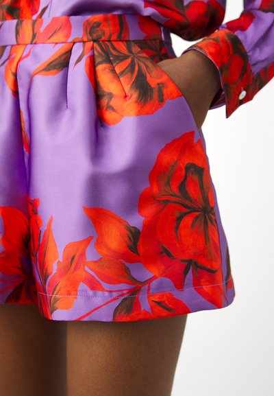 Purple fabric shorts featuring a vibrant red floral pattern, pleated front, side pockets, and a smooth satin-like texture.