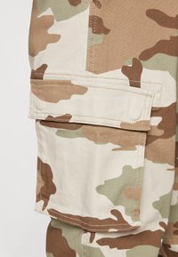 Camouflage cargo-broeken in bruin, groen en beige, met een grote zijzak en een stevige stof met zichtbare stikseldetails.