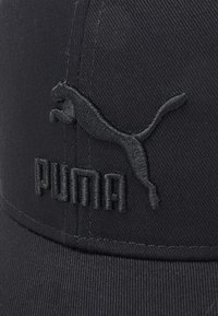 Cappello nero con tessuto testurizzato. Presenta un logo Puma nero ricamato e il nome sul fronte, evidenziando un design elegante e minimale.