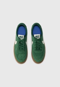 Baskets en suède vert avec le swoosh blanc de Nike, semelle extérieure en caoutchouc marron et doublure de chaussette bleue. Elles disposent de laçage traditionnel et d'un col rembourré.