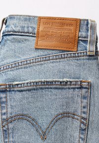 Poche arrière de jean en denim bleu clair avec étiquette en cuir de la marque Levi Strauss cousue au-dessus, montrant une couture classique et une texture de tissu délavée.