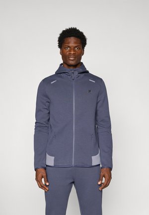 Mørkeblå zip-up jakke med hætte, kontrasterende grå detaljer, to sidelommer og et glat, struktureret stof. Logoet på brystet er synligt.
