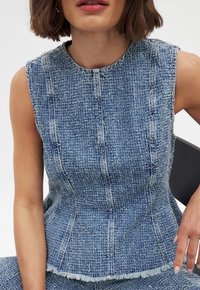 Denim mouwloos topje met een aangesloten lijfje. Heeft een gestructureerde blauwe stof, een ronde hals en een rafelige zoom, wat de gestructureerde uitstraling benadrukt.