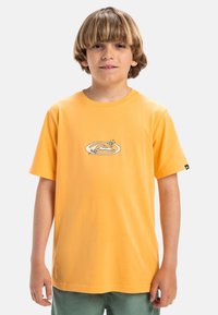 Camiseta de algodón amarilla con un logo circular en azul y naranja con acentos florales, de mangas cortas y corte relajado.