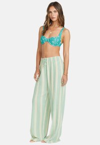 Haut de bikini floral turquoise avec de larges bretelles, associé à un pantalon large rayé vert clair avec une taille à cordon de serrage. Tissu doux et léger.
