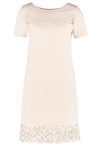 Krátký béžový šaty z měkké tkaniny, které mají krajkovou aplikaci na hrudi a vlnitý krajkový lem na spodu.