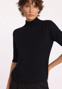 Czarny sweter z krótkim rękawem o wysokim ściągaczu i gładkiej teksturze. Posiada luźny krój oraz prosty brzeg.
