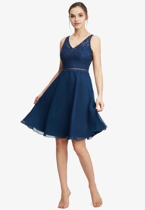 Robe bleu marine avec un corsage en dentelle et une jupe évasée et transparente. Elle possède un décolleté en V et une taille cintrée avec une délicate bordure.