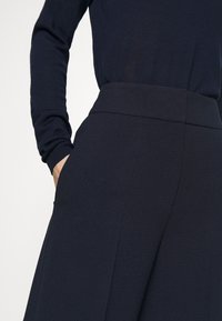 Marina blå byxor i ett slätt tyg med hög midja, featuring sidofickor och en skräddarsydd passform längs benen.