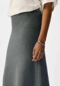 Gray, ribbed long skirt with a fitted waistband, paired with a white loose top, featuring a silver bracelet on the model's wrist.