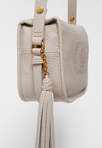 Sac à main en cuir beige avec une finition texturée, de forme rectangulaire, équipé de quincaillerie dorée, d'une bandoulière réglable, et d'un détail en frange sur le côté.