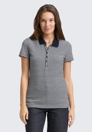 Polo rayé bleu marine et blanc avec des manches courtes et un col; comporte une patte de boutonnage. Porté avec un pantalon en denim foncé.